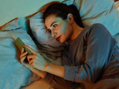 Top view portrait of smiling adult woman using smartphone in bed at night reading text messages and scrolling social media